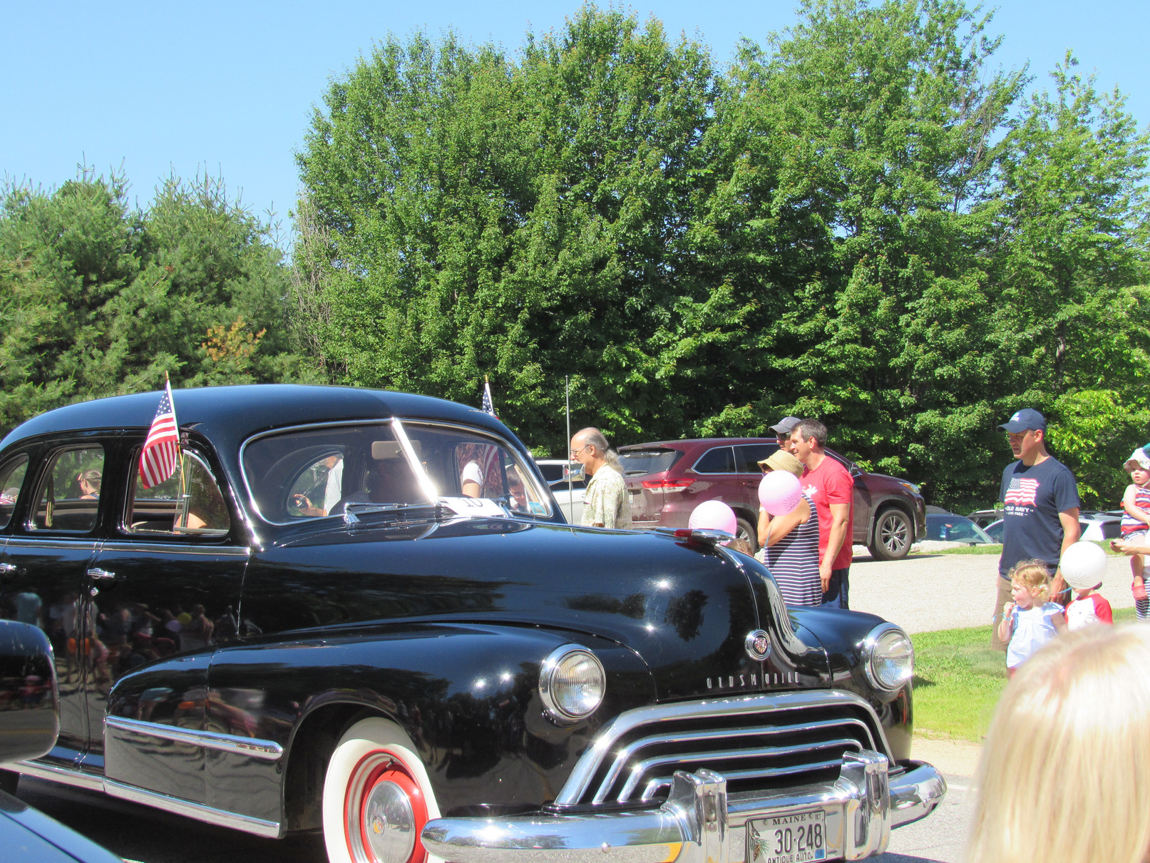 Antique passenger car passing parade spectators at the Fourth of July parade.