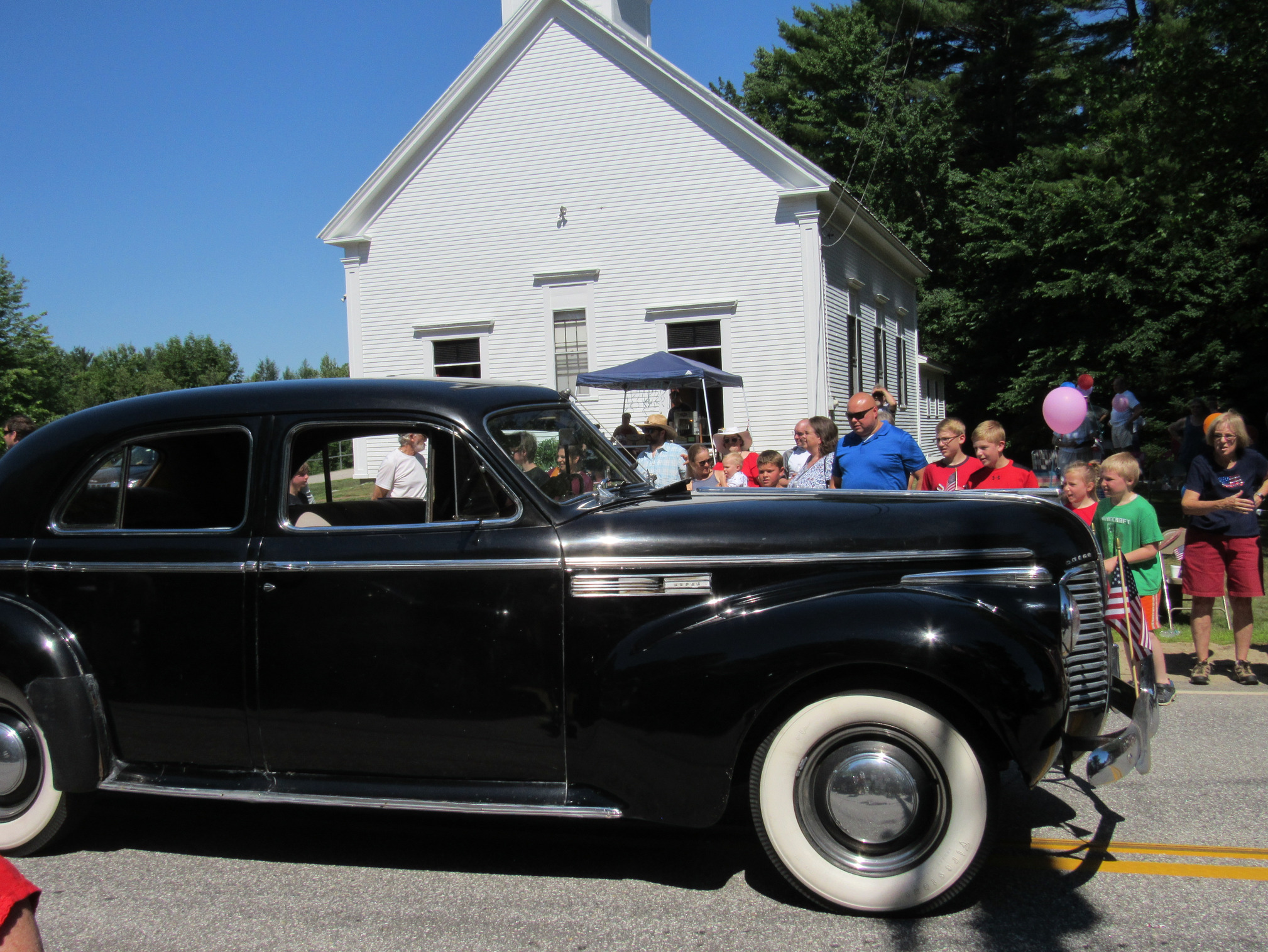 Antique passenger car passing parade spectators at the Fourth of July parade.