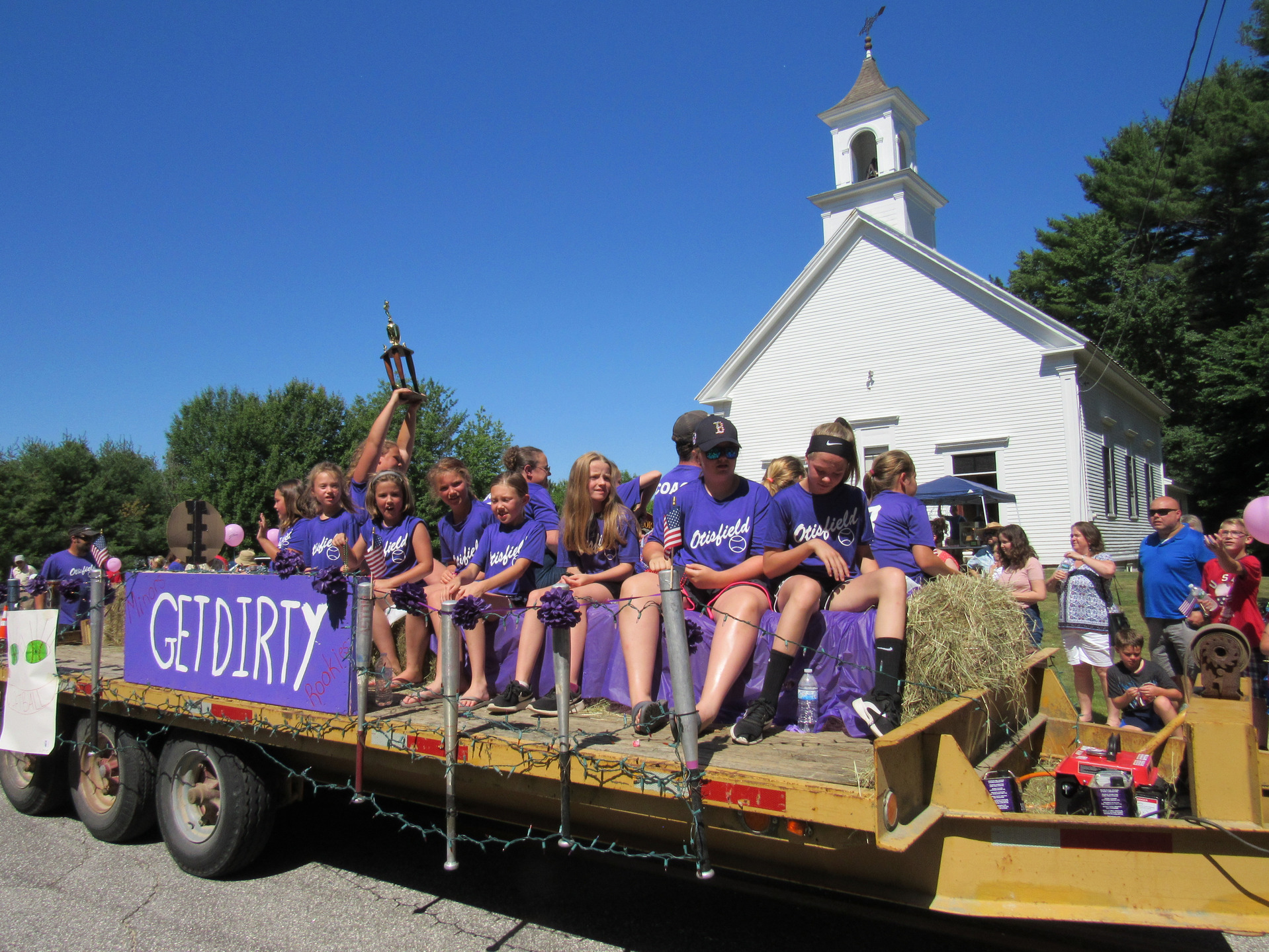 Softball team float with a trophy and GET DIRTY banner at the Fourth of July parade.