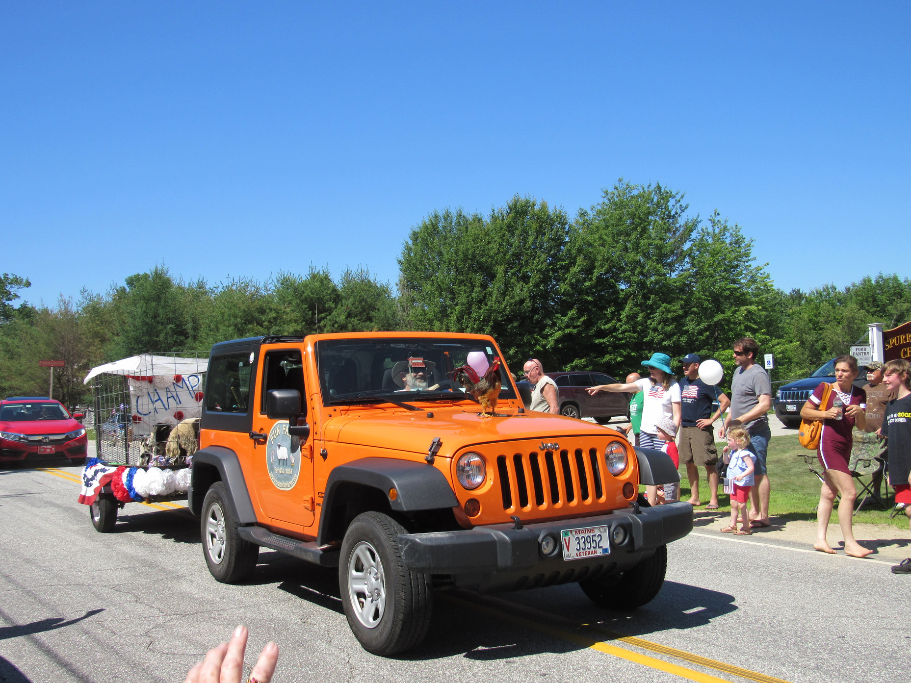Orange Jeep towing a decorated animal trailer at the Fourth of July parade.